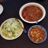 We have a side of cooked cabbage and two sauces for our noodles. One sauce has fried chicken and the other sauce has fried egg. 