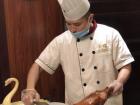 One of the chefs at the restaurant preparing peking duck by shaving it into smaller, oval-shaped slices
