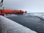 An Autonomous Underwater Vehicle (AUV) on the side of the vessel, above the ice