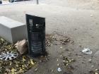 Overflowing trash can with trash surrounding it, including a car rim