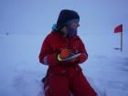 Carrie kneels in the snowy surface of the sea ice while writing down observations about the ice floe (Photo: Anika Happe)