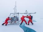 A group of atmospheric scientists push a fluxsled, which measures atmospheric properties of the air and ice surface over a melt river on the floe