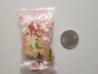 A single cracker individually wrapped in plastic placed next to a US quarter for size comparison