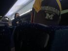 A man wearing a hat from my college, UofM, on one of the larger buses