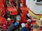 Workers on the drill floor attach a new drill bit (the shiny, silver part) to the bottom of the drill pipe