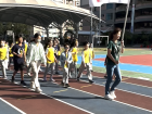 Third-grade students and a teacher carry a flag that says the school name and their grade