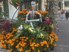 A catrina made of paper mache, surrounded by marigolds