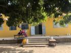 The teenage girls sit on a bed/table on the porch of the main house. This is a gathering spot to socialize, fold laundry, and eat meals throughout the day.