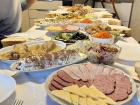 A different family meal with cold cuts, crepe cake, fish, olives and pickled carrots