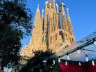 The sunlit exterior of the Sagrada Familia with a Christmas market stall in front