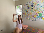 Taking a photo of my friend taking a photo of me in my guest room; behind me are lots of drawings from the kids in town