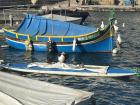 A traditional Maltese fishing boat with some ducks hanging out nearby
