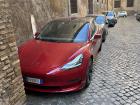 A modern electric Tesla parked on a narrow Roman street; new technology blending with the city’s ancient setting