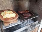 A grill with numerous meats, potatoes and corn