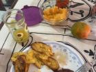 A breakfast plate that consist of scrambled eggs, beans, plantains, orange watermelon (in the bowl), and a variation of a mandarin with orange juice